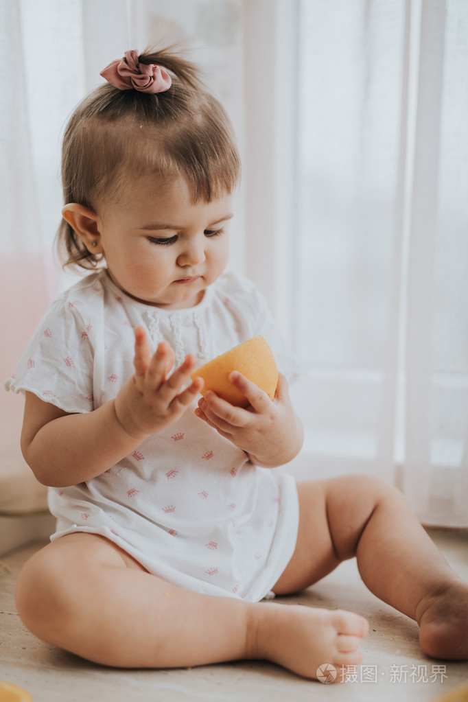 可爱的小宝贝女孩在厨房的桌子上吃柑橘类水果富含维生素和滑稽可爱的