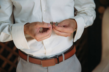 新郎袖扣的双手。优雅绅士的衣服，白色的衬衫和棕色腰带