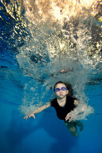 快乐的小女孩，游泳和打水下气泡在蓝色背景上