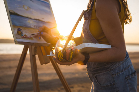 年轻女子艺术家画风景画在露天沙滩上