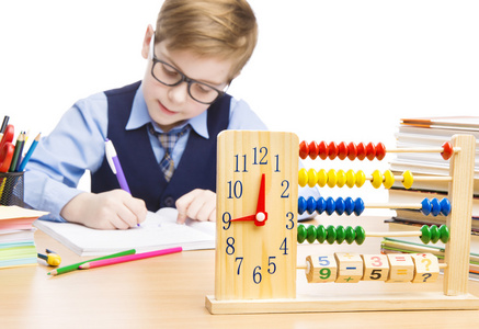 男孩在学校写作业，桌上放着算盘和教育时钟