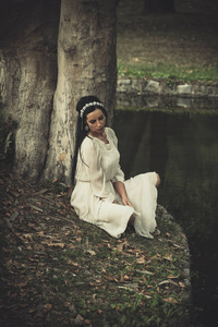 浪漫的打扮和头发装饰的年轻女子坐在湖边