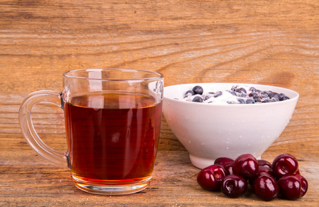 杯茶甜樱桃和蓝莓在木制的白碗图片