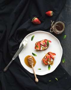 法国吐司与草莓 奶油奶酪 蜂蜜和薄荷光陶瓷板在黑色背景上