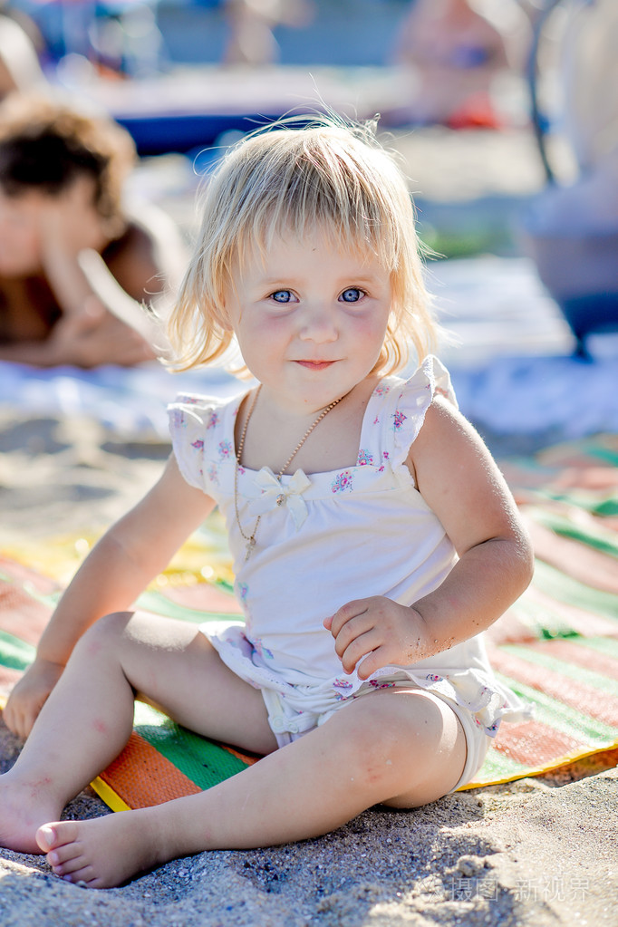 一个小女孩坐在沙子和微笑的海滩上