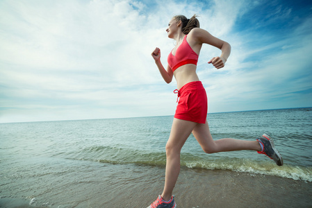 年轻的女士在阳光灿烂的夏天砂沙滩上运行。锻炼。慢跑