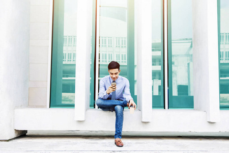 年轻的商人使用或工作在智能手机和坐在外部办公大楼, 社会沟通技术的商业理念, 现代男性的生活方式