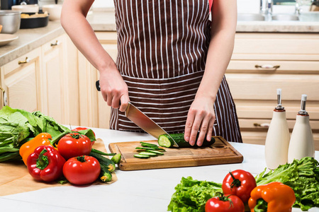 年轻的女人在家里的厨房里做饭。一个女人用小刀切黄瓜和蔬菜