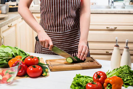 年轻的女人在家里的厨房里做饭。一个女人用小刀切黄瓜和蔬菜