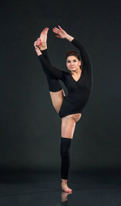 运动的舞蹈女孩在黑色背景和持有一英尺, 而伸展