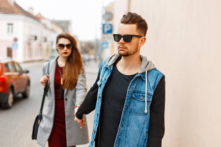美丽时尚的年轻夫妇带着太阳眼镜的行走在城市的时尚衣服。恋人的手