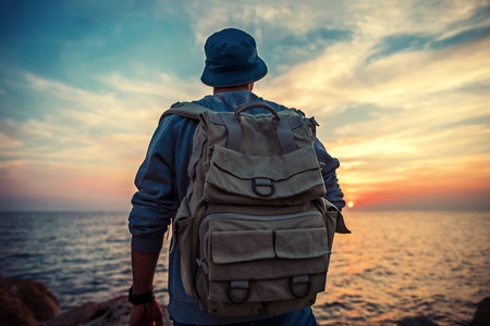 看着日落的天鹅与附近海很远的地方看着地平线在日落时分的背包旅行者