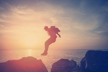 夕阳奔跑带着背包的勇敢的人在夕阳下的海洋附近的岩石上奔跑照片