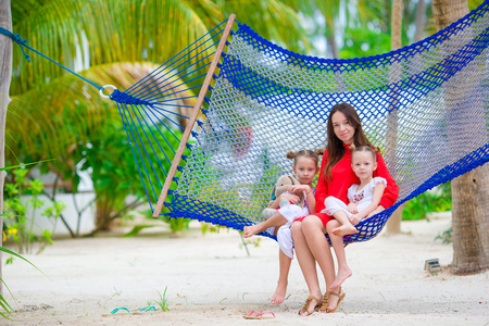 母亲和两个孩子坐在吊床上热带海滩上