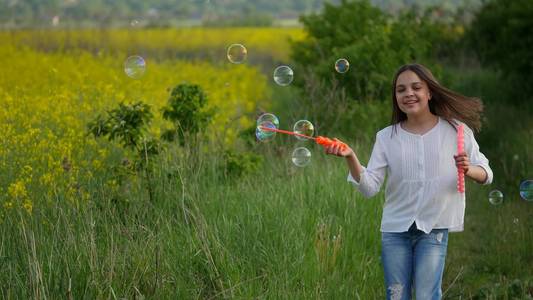 快乐的小女孩，夏季绿色的草地上玩肥皂泡泡之间
