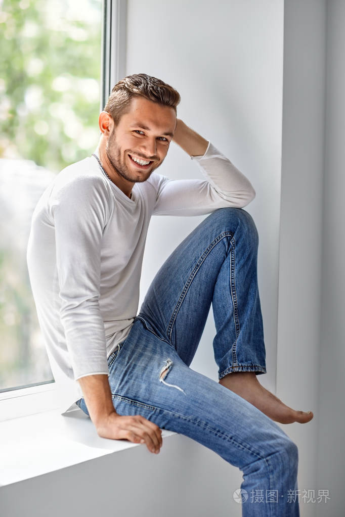 快乐的男人微笑着放松在窗台上