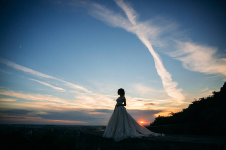 年轻的女孩穿着婚纱时对城市的背景下，在日落时