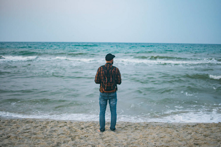 一个年轻的白人游客男子站海洋背景黎明时分。旅游和生活方式的概念