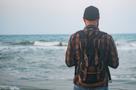 一个年轻的白人游客男子站海洋背景黎明时分。旅游和生活方式的概念