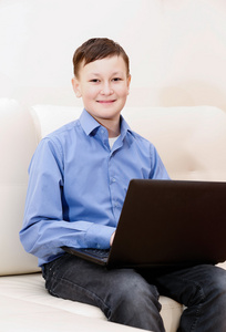 小男孩坐在沙发上用笔记本电脑