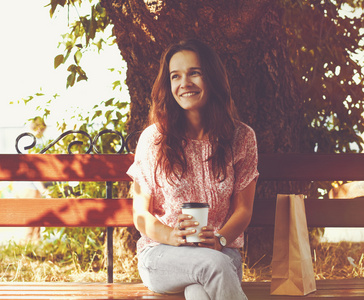漂亮小女孩微笑着坐在长椅上与早晨喝咖啡