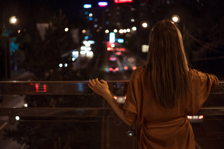 年轻女子看视图夜间城市道路从桥