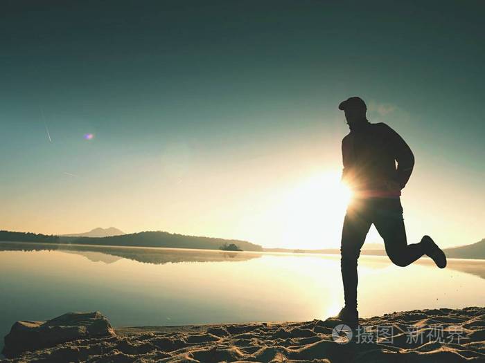 人行使和日出时在湖滩上伸展健康的生活方式孤独的年轻健身人行使在