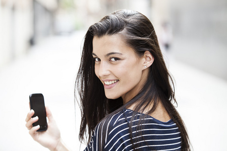 幸福的女人在大街上不专心的背景使用智能手机