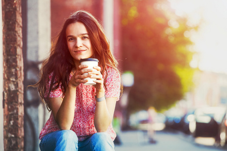 漂亮小女孩微笑着坐在街与早晨喝咖啡