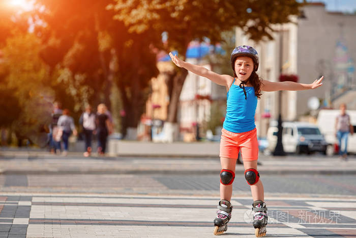 有趣小的漂亮的女孩骑在一个公园里的头盔旱冰