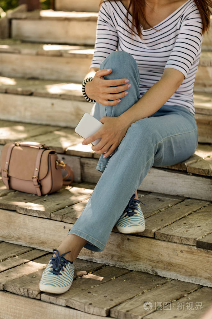 蓝色的牛仔裤和条纹的运动鞋的年轻女子坐在老早饭中规中矩