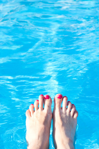 在背景上游泳池水的红指甲的脚