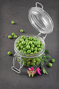 健康的食物。鲜绿色豌豆在打开玻璃罐与粉红色花的香豌豆
