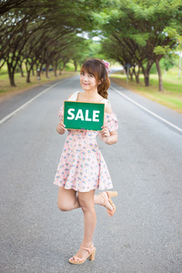 可爱的女人手拿着绿板标志与文本出售路 树 微笑女模特