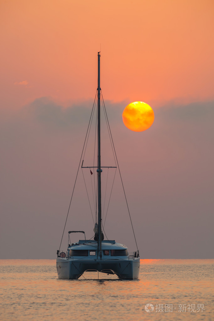 美丽的双体船航行在海上日出的背景