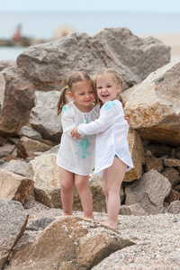 孩子们在海滩上。双胞胎站对抗石头和海水