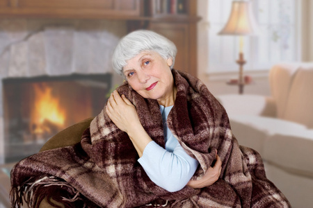 快乐的美丽的老妇坐在房间里覆盖着一条毯子。妈妈。祖母