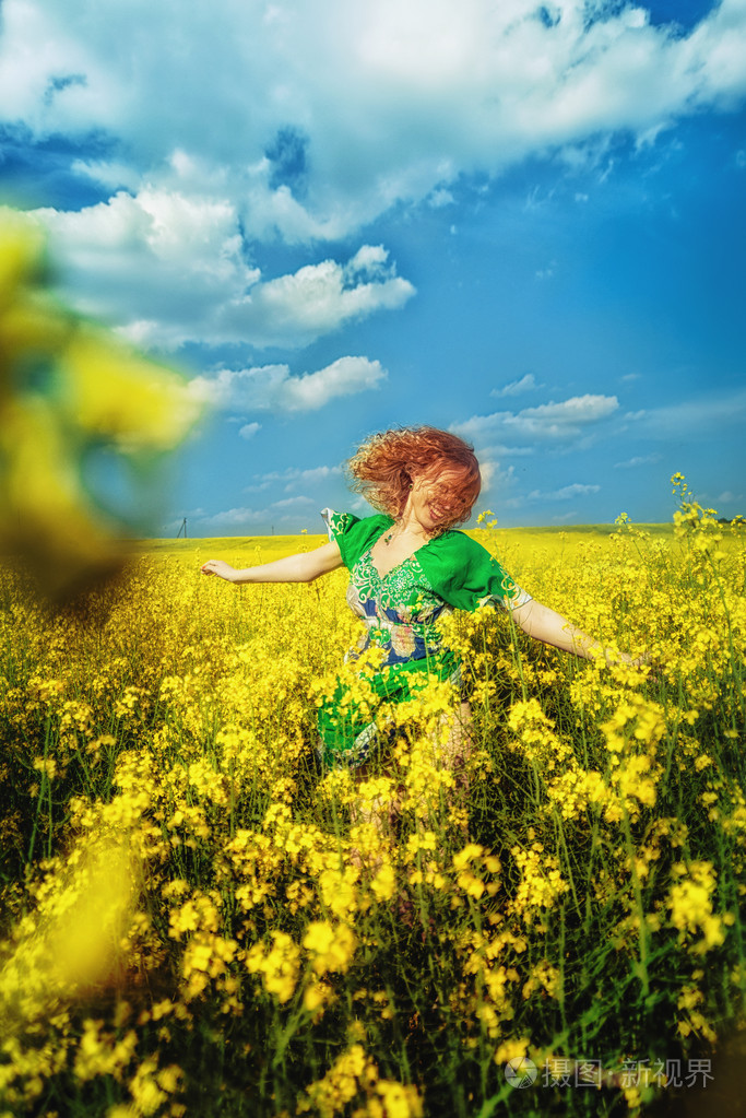 快乐红头发的年轻女孩,穿着绿色的跳跃在黄色字段