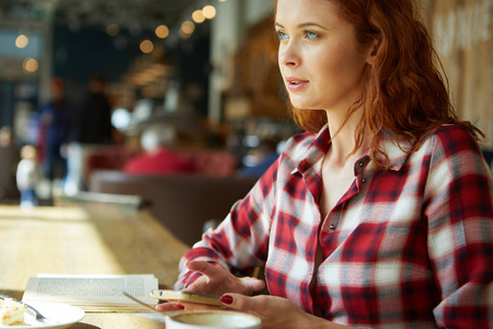 红头发的女人在咖啡馆里看书。城市休息概念