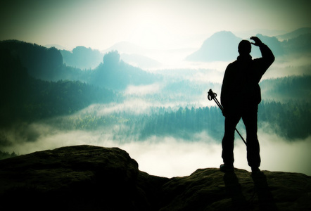在洛矶山脉有雾的日子。旅游与剪影手杆。徒步旅行者站在岩石看法点上方迷雾笼罩的山谷