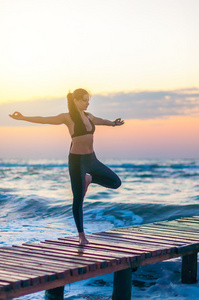 年轻女子正在练习瑜伽的第一缕阳光照在海洋背景上。健康，体育概念的生活方式