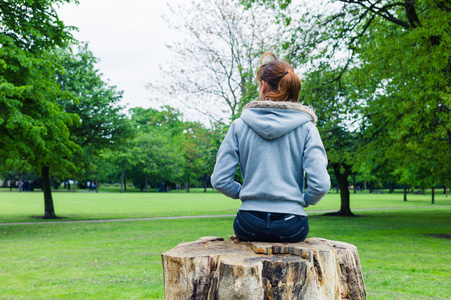 年轻的女人坐在公园的树干