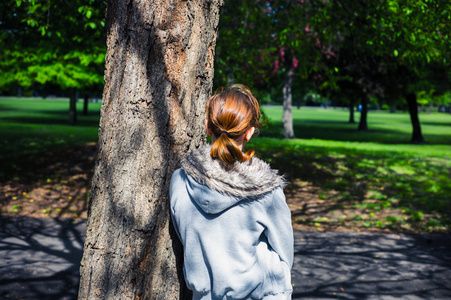 年轻女人靠在公园里的树
