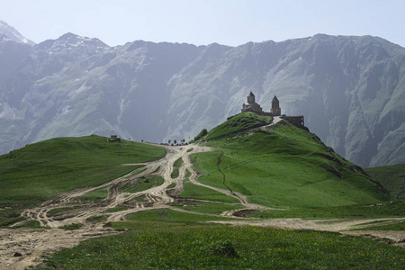 在格鲁吉亚山背景上绿草与如诗如画的山间公路上夏天山上三位一体 Gergeti 三一教堂