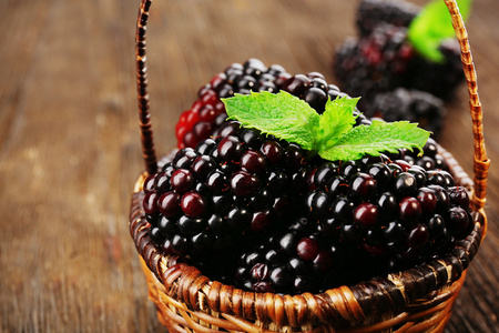 熟透的黑莓，绿色的叶子在柳条篮子里的木桌前，特写