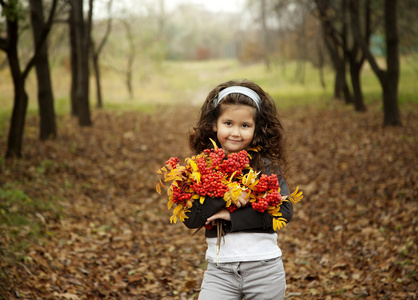 卷曲的黑发坐在秋天的树林与 rowanberry 一束可爱的小女孩