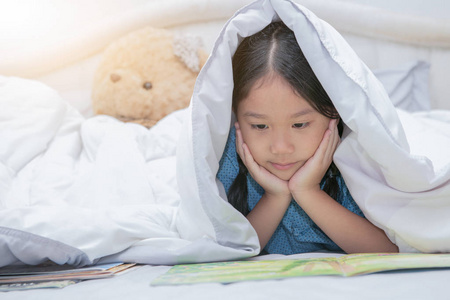 可爱的小亚洲女孩读童话书的下毯子