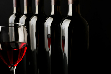 红葡萄酒杯瓶成一排在黑色背景上，反对关闭
