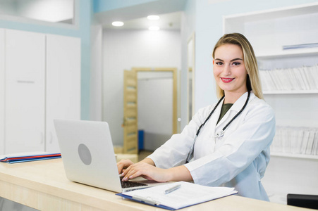 微笑穿磨砂和医院接待处工作的女医生，她是写一份关于剪贴板的医疗报告，安排预约