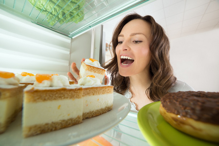 吃一块蛋糕从冰箱里的女人